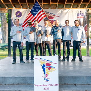 Seven men standing on a stage in front of a colorful banner holding the flag of the United States of America