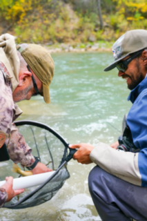 Two men extracting a fish from a net on a greenish blue river