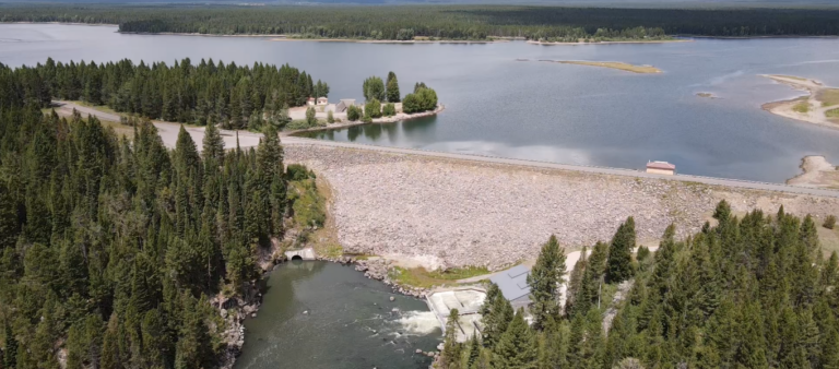 An aerial view of Island Park Dam. The reservoir sits behind it and the river flows below it.